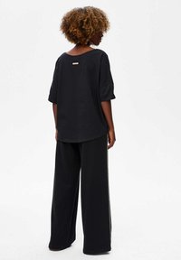 Black oversized sweatshirt with short sleeves and a scoop neckline, paired with black wide-leg pants featuring a side stripe detail.