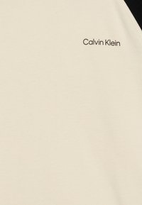 Platno od pamuka boje krem s glatkom teksturom i crnim akcentom. Sadrži mali, otisnuti 'Calvin Klein' logo u crnoj boji.
