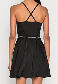 Svart klänning med ett åtsittande liv och tunna, korslagda axelband samt en utsvängd kjol. Elastisk midja med "Calvin Klein Jeans"-logotyp.