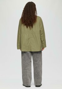 Veste en coton vert olive avec une coupe décontractée et des manches longues, dotée d'une taille cintrée. Associée à un pantalon à jambes larges gris en denim.