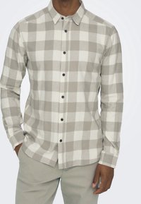 Grijze en witte geruite shirt met een knoopsluiting kraag, lange mouwen en marineblauwe knopen. Zachte textuur en een losse pasvorm.