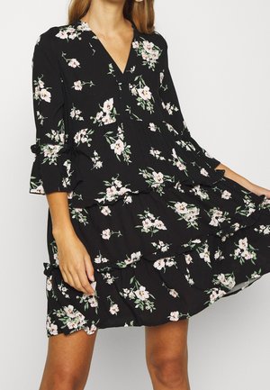 Robe noire à motifs floraux avec un décolleté en V, des manches trois-quarts, des couches froncées et des motifs de fleurs blanches et roses. Tissu doux et coupe décontractée.