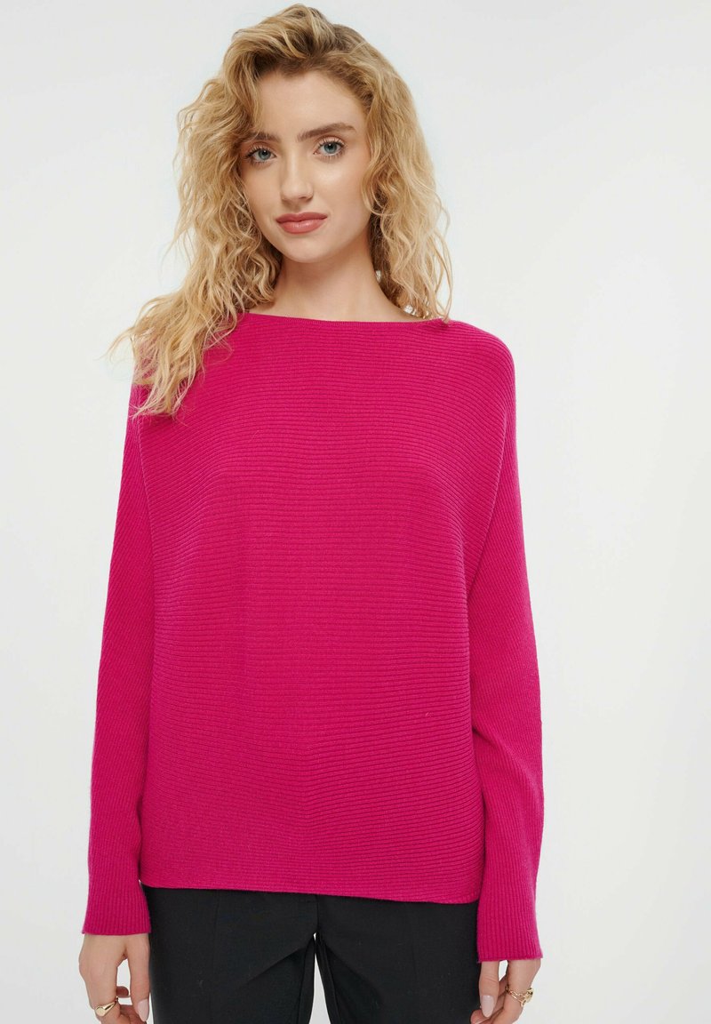 Fuchsia geripptes Sweatshirt mit weitem Bootsausschnitt und langen Ärmeln, das eine lockere Passform und eine weiche Textur aufweist. Kombination mit schwarzen Hosen.