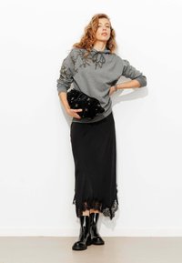 Sweat-shirt gris avec des détails complexes en perles, pochette en satin noir, jupe noire avec bordure en dentelle et bottines noires brillantes.