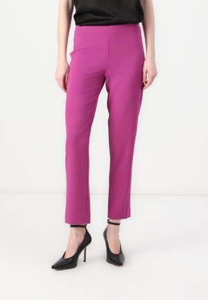 Aansluitende, enkel-lange broek in felroze stof. Gladde textuur met hoge taille. Gecombineerd met zwarte hoge hakken.