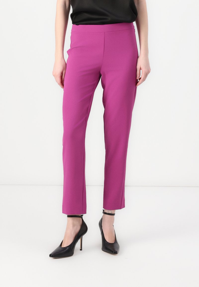 Pantalon ajusté, longueur cheville, en tissu rose vif. Texture lisse avec une taille haute. Associé à des chaussures à talons hauts noires.