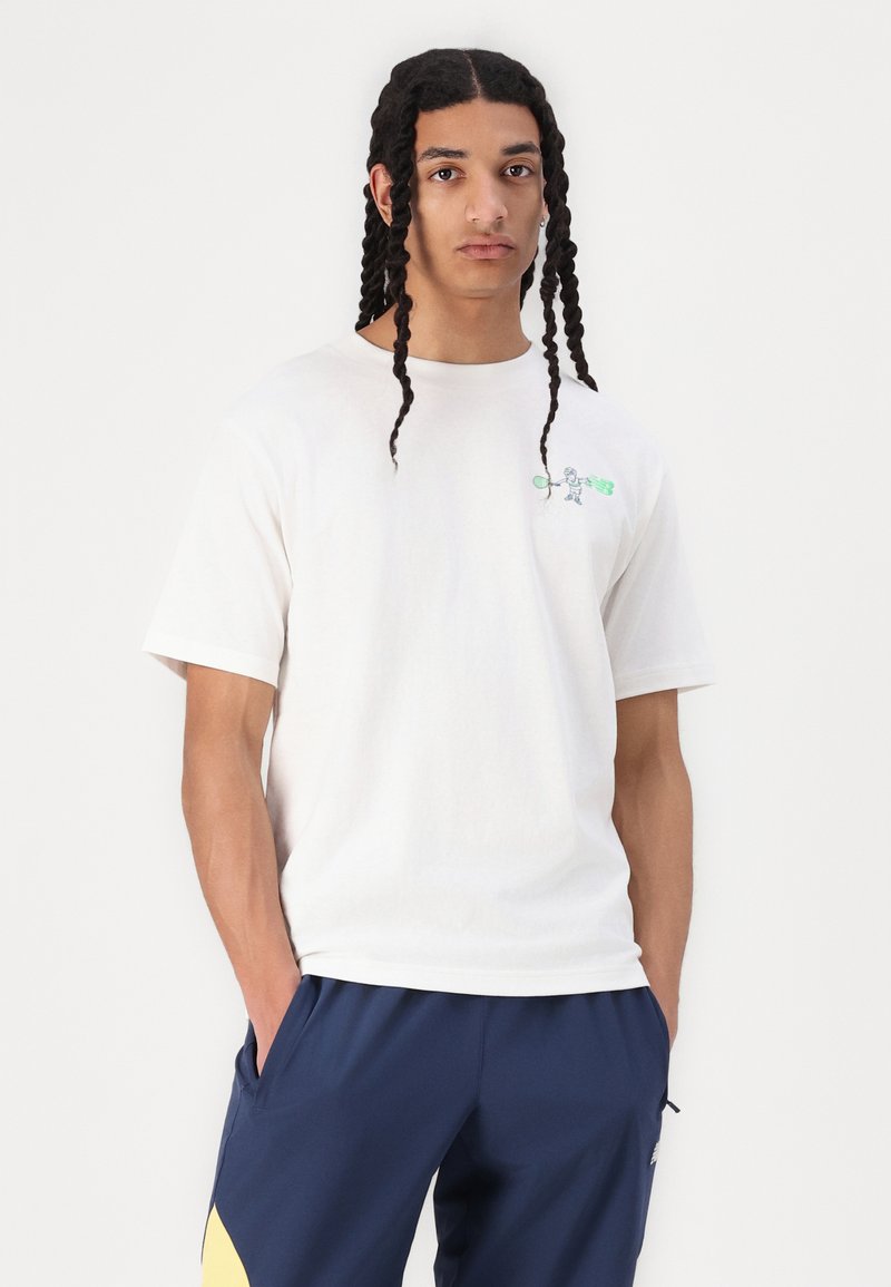 T-shirt crème, à manches courtes, avec un col rond et un motif de robot brodé sur la poitrine. Tissu en coton lisse.