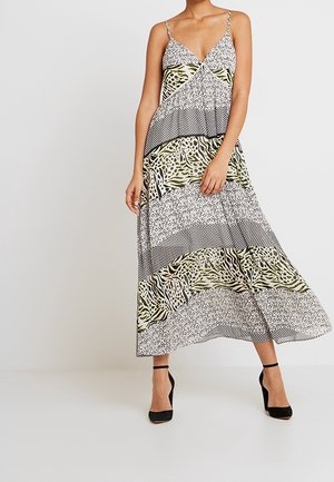 Kvinde iført en ærmeløs maxi-kjole med V-hals i blandede dyre- og geometriske mønstre, kombineret med sorte ankelrem-sandaler.