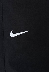 Black athletic pants made of stretchy fabric, featuring a white Nike swoosh logo on the left side. Smooth texture, fitted design.