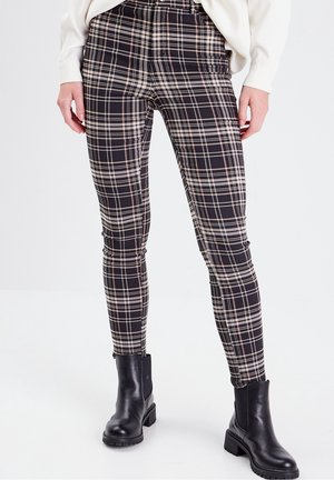 Pantalons à carreaux noir et blanc avec une coupe ajustée, présentant des nuances de rose. Assortis à des bottines noires. Tissu texturé avec élasticité.