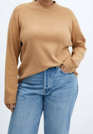 Pull en maille beige avec un col montant et des manches longues, associé à un jean en denim bleu clair avec une poche avant et une fermeture à bouton.