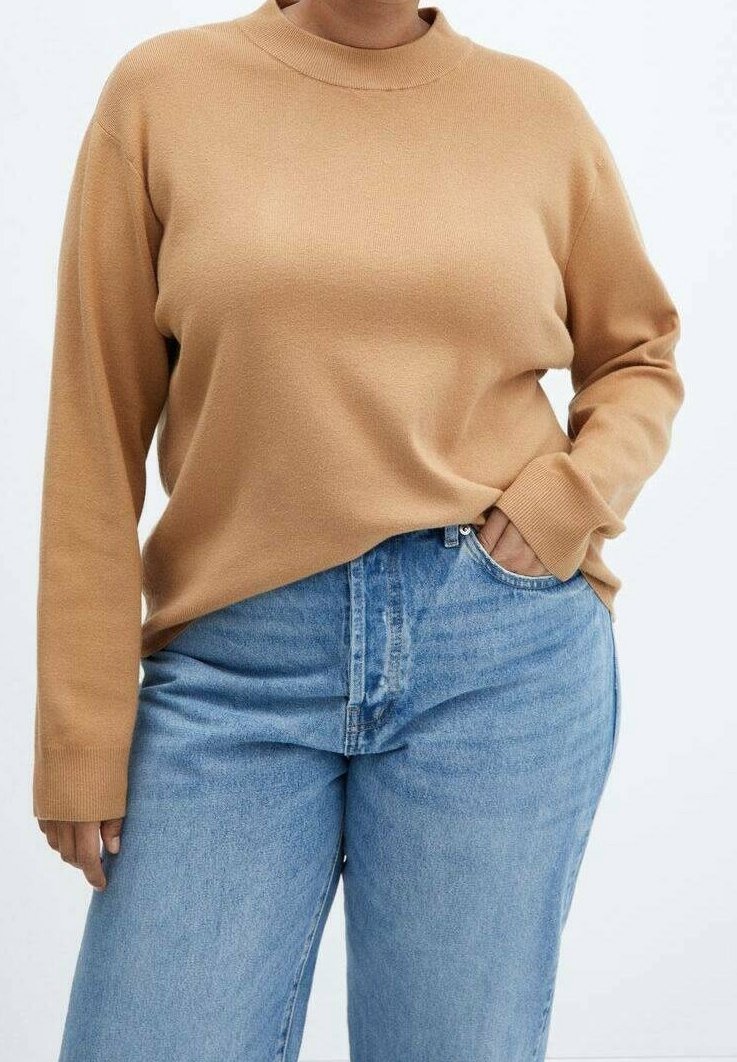 Suéter de punto beige con un cuello alto y mangas largas, combinado con jeans de mezclilla azul claro que presentan un bolsillo frontal y un cierre de botón.