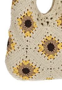 Koukuttu valkoinen olkalaukku, jossa on ruskea-keltainen auringonkukkakuosi. Laukussa on pyöreä muoto ja avoin yläosa helppoa käyttöä varten.