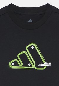 Fekete póló, amelyen zöld versenypálya grafika látható, fehér versenyautóval és számozott szakaszokkal (01, 02, 03).