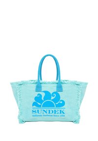 Bolso tote azul claro con un borde de flecos, que presenta un gran gráfico de un sol azul y el texto "SUNDEK Ropa de Surf Auténtica Desde 1968".