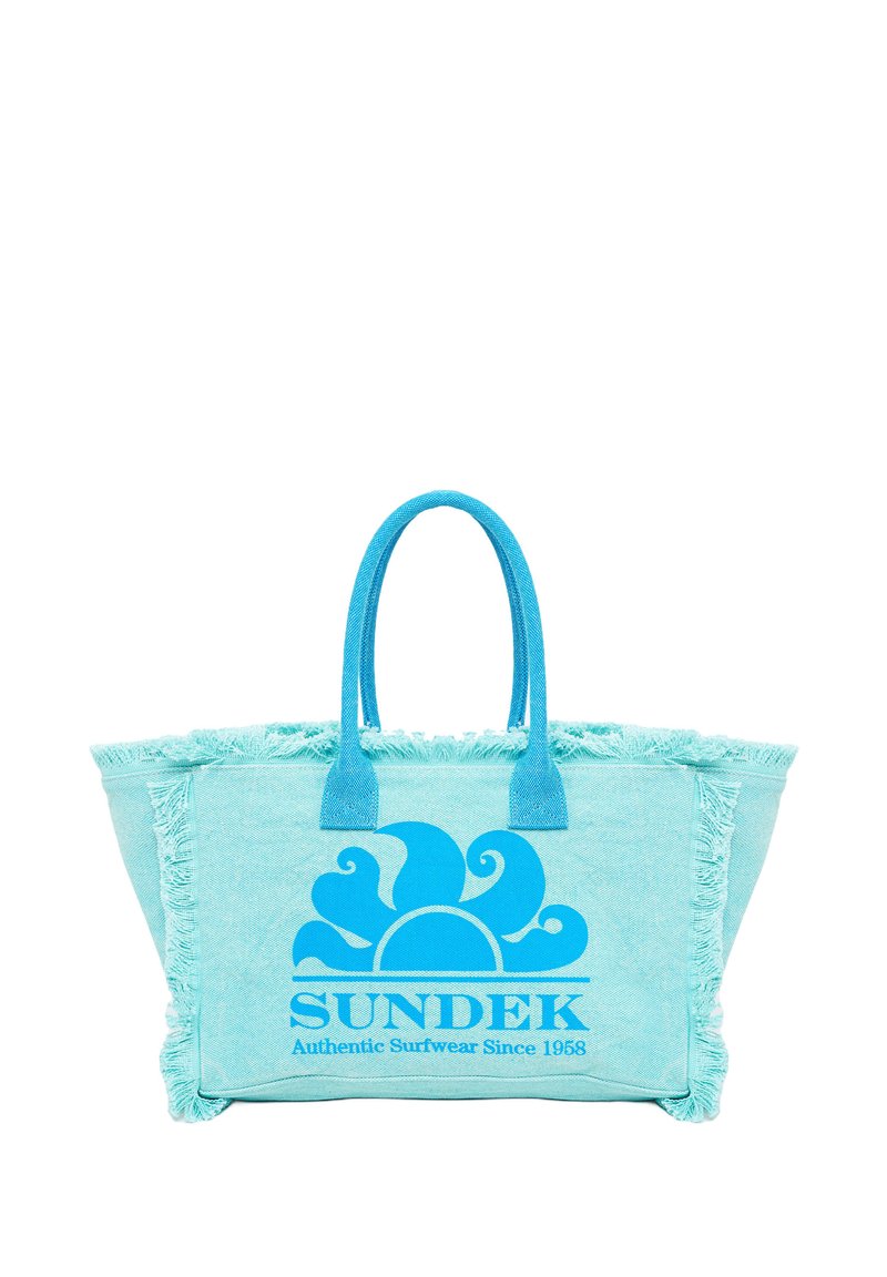 Bolso tote azul claro con un borde de flecos, que presenta un gran gráfico de un sol azul y el texto "SUNDEK Ropa de Surf Auténtica Desde 1968".