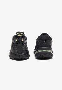 Scarpe sportive nere con parte superiore in rete e sintetico, dotate di un motivo texturizzato, dettagli dorati e una suola intermedia di colore verde.