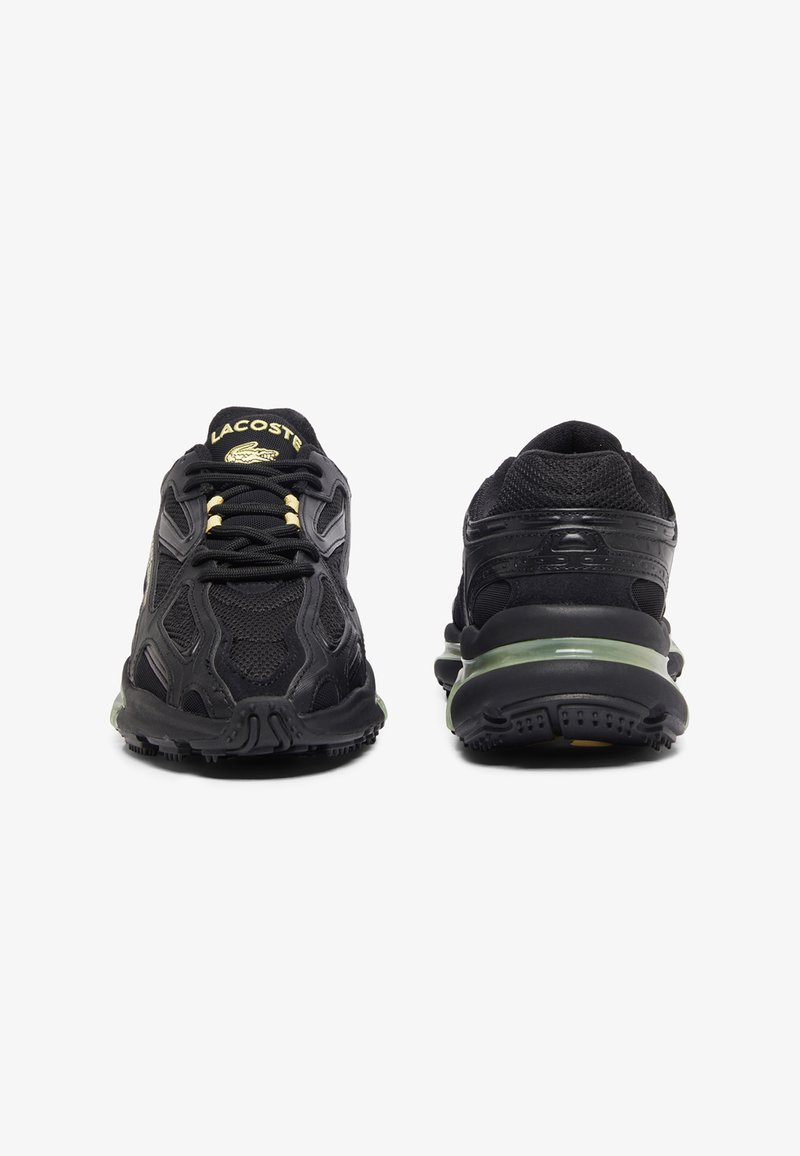 Baskets de sport noires avec une tige en mesh et synthétique, dotées d'un motif texturé, d'accents dorés et d'une semelle intermédiaire teintée de vert.