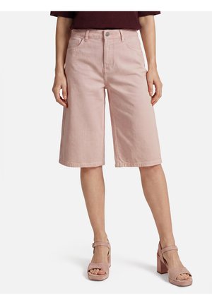 Model draagt lichtroze, wijde knielange shorts met voorzakken en bijpassende roze sandalen met hoge hakken.