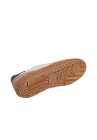Suela de zapato con material de goma, que presenta un patrón en panal, color marrón y surcos distintivos. Acentuada con secciones en beige claro y gris oscuro.