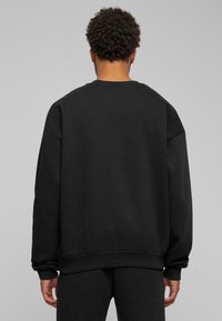 Felpa nera a girocollo, vestibilità ampia, polsini e orlo rib rib, texture morbida, presenta spalle cadenti e dettagli di design minimali.