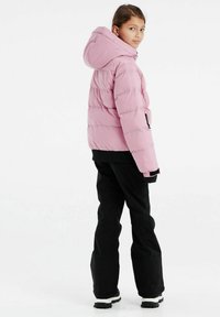 Giacca gonfiabile rosa con cappuccio, design trapuntato e polsini elastici, abbinata a pantaloni neri e calzature robuste, vista dalla schiena.