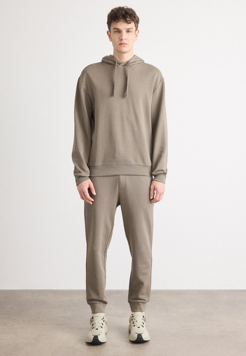 Hanorac cu glug�ă și pantaloni jogger asortați dintr-un material moale, de culoare taupe. Are mansete și tiv cu dantelă, cu minimal branding pe piept.