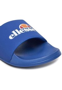 Niebieskie klapki z szerokim paskiem, na którym znajduje się białe logo. Podeszwa ma teksturowaną powierzchnię dla lepszej przyczepności, a materiał wydaje się gładki i trwały.