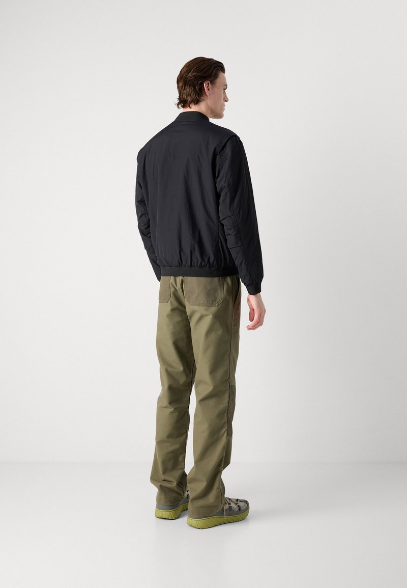 Czarna kurtka bombowca o gładkiej fakturze, z zapięciem na zamek i elastycznymi mankietami, zestawiona z oliwkowymi spodniami cargo z bocznymi kieszeniami.