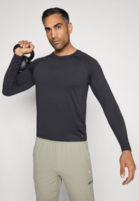 Melna garām piedurknēm paredzēta sporta krekla, izgatavots no gludas, elastīgas auduma. Tam ir raglanu piedurknes un pieguļoša forma.