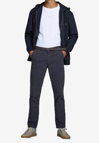 Sudadera con cremallera en azul marino oscuro, camiseta blanca, pantalones grises con bolsillos y zapatillas ligeras en gris claro con superficie texturizada y suela de goma marrón.