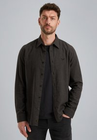 Donkergrijze button-up shirt met een kraag, gemaakt van textiele stof, gecombineerd met een zwart T-shirt eronder, gedragen met zwarte spijkerbroeken.