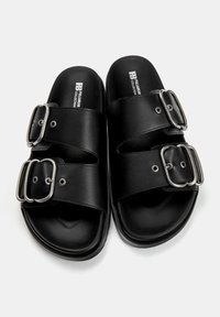 Schwarze Rutschsandalen mit zwei breiten Riemen und metallischen Schnallen. Hergestellt aus glattem Material mit einer flachen Sohle und gepolstertem Fußbett.