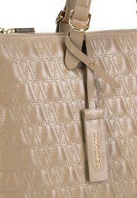 Beżowa skórzana torebka z wytłoczonym trójkątnym wzorem, złote elementy wykończeniowe, regulowany pasek i zawieszka z logo.