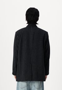 Black pinstriped blazer with a tailored fit, notched collar, and a textured fabric. The back features a vent and long sleeves.