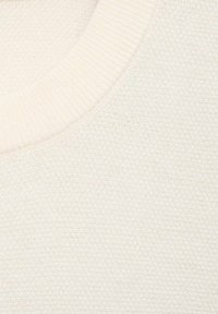 Jasno beżowy sweter z materiału o teksturowanym splocie i ściągaczem przy dekolcie. Miękki materiał z delikatnym połyskiem.