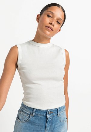 Top blanco sin mangas con un cuello alto, hecho de una tela suave, combinado con pantalones vaqueros de mezclilla azul claro que presentan bolsillos frontales y detalles de costura.