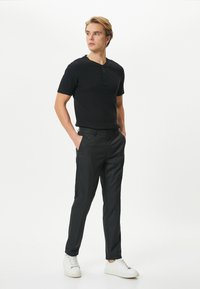 Camisa henley negra de manga corta con un acabado texturizado, combinada con pantalones negros ajustados y zapatillas blancas. Diseño limpio y moderno.