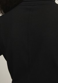 Černý svetr s žebrovanou strukturou. Design zahrnuje vysoký límec a šev vedouc�í svisle uprostřed zad.