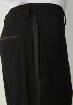Black formal trousers with a satin side stripe and waistband, shown from the waist to mid-thigh on a person wearing a white shirt.
