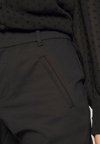 Černé elegantní kalhoty s hladkou matnou texturou, s boční kapsou a rovně střiženými nohavicemi. Pás je nenápadný.