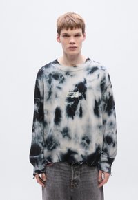 Μπλούζα tie-dye σε ασπρόμαυρο με μακριά μανίκια, ριμπ μανσέτες και σκισμένο τελείωμα. Διαθέτει λογότυπο HUGO στο στήθος.