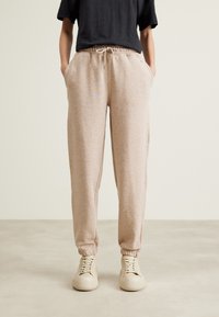 Jasnobeżowe spodnie dresowe wykonane z miękkiego materiału, z elastycznym pasem i sznurkiem, bocznymi kieszeniami oraz zwężanymi ściągaczami.