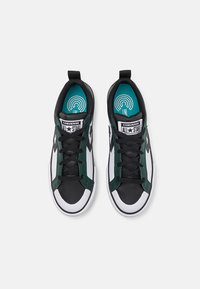 Zapatillas sintéticas en negro y verde con acentos en blanco. Las características incluyen cierre con cordones, punta redondeada y logo en la lengüeta.