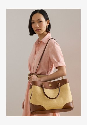 Kvinde i en pink kjole, der holder en beige og brun læderbesat shoppertaske med gyldent RLL-logo på skulderremmen.