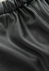 Sort faux læder stof med en samlede elastisk talje og tekstureret overfladedetalje.