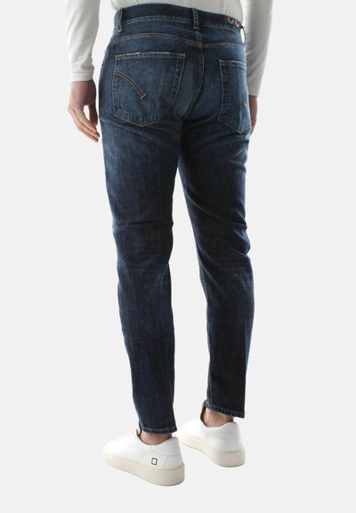 Jeans in jeans scuro con una vestibilità affinata, tasche posteriori con dettagli di cucitura, abbinati a sneaker bianche.