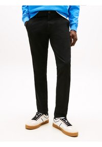 Černé kalhoty úzkého střihu vyrobené z elastické tkaniny; doplněné bílými a béžovými teniskami s černými akcenty.