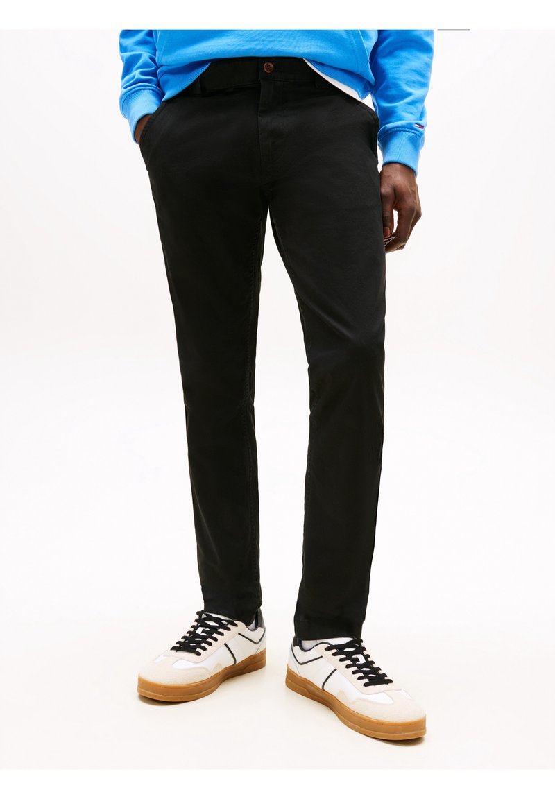 Černé kalhoty úzkého střihu vyrobené z elastické tkaniny; doplněné bílými a béžovými teniskami s černými akcenty.