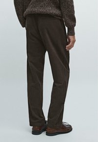 Mørkebrune corduroy bukser med straight-leg snit, der har baglomme og en glat tekstur, parret med brune snørebåndssko.
